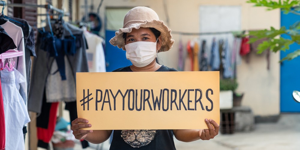 Gewerkschafterin hält ein Schild hoch auf dem #payyourworkers steht