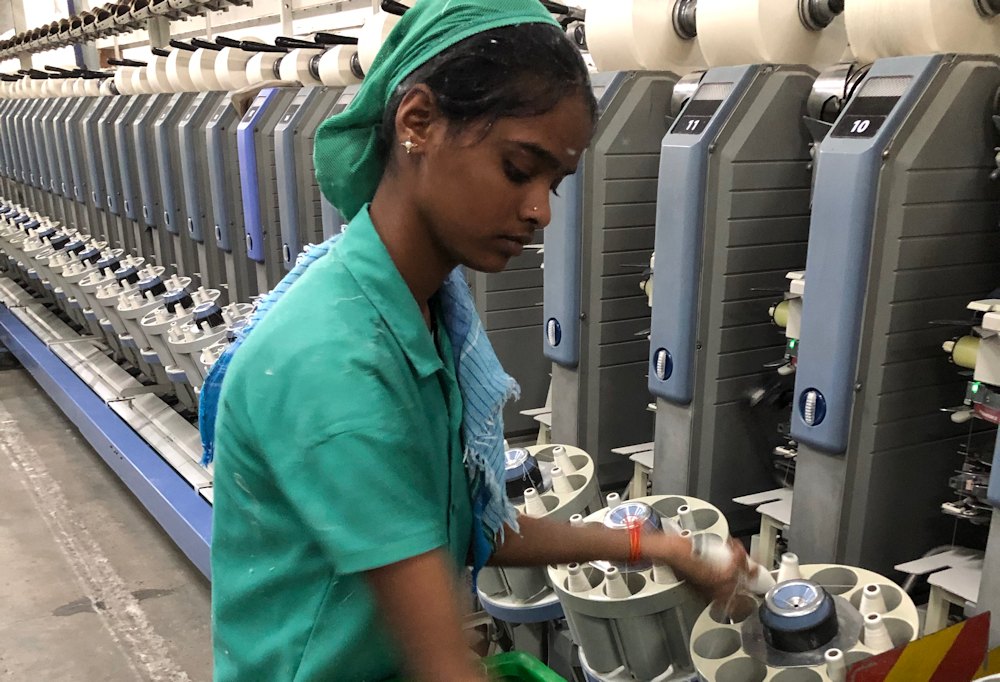 Junge Textilarbeiterin legt Fadenspulen in einer Spinnerei nach